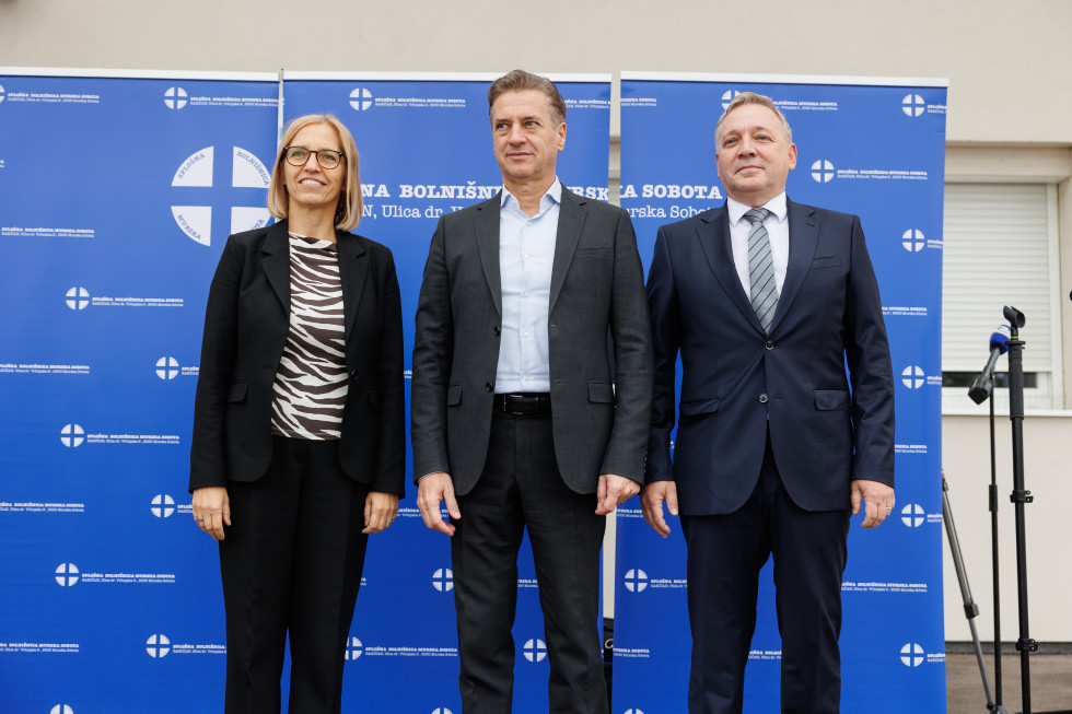 Predsednik vlade, ministrica za zdravje in moški stojijo na odru.