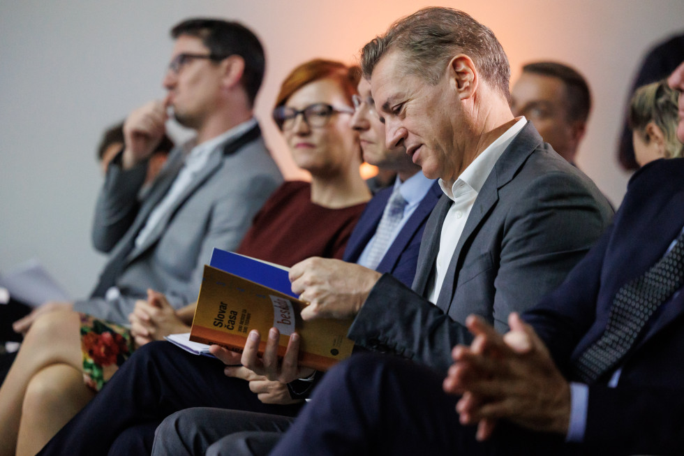 Predsednik vlade sedi v prvi vrsti in bere knjigo Slovar časa