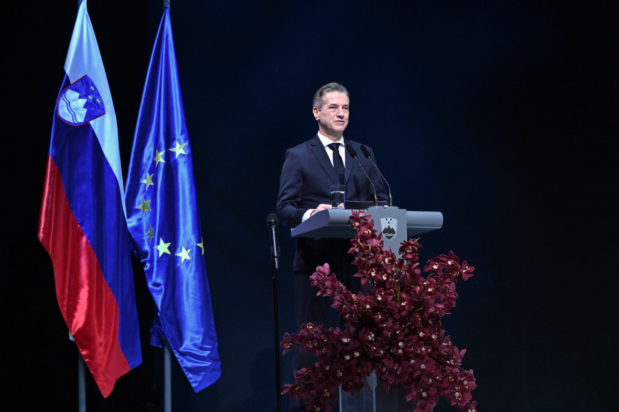 moški za govorniškim pultom, zadaj zastave