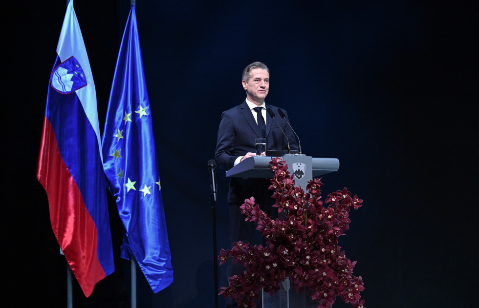 moški za govorniškim pultom, zadaj zastave