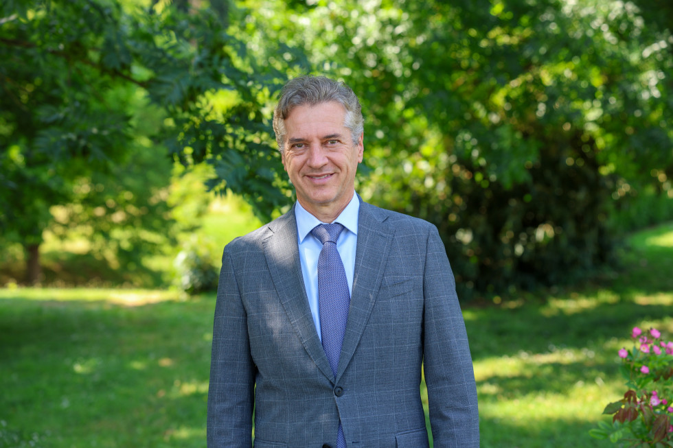 Predsednik vlade stoji in se smeji sredi zelenega parka, obdan z drevesi in travo