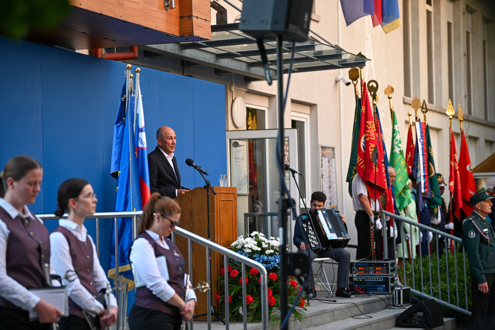 moški za govorniškim odrom med zborom in harmonikarjem