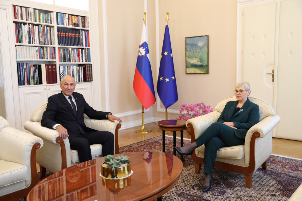 Janez Janša and Nataša Pirc Musar are sitting in armchairs; there is a table in front of them, and flags are visible in the background.