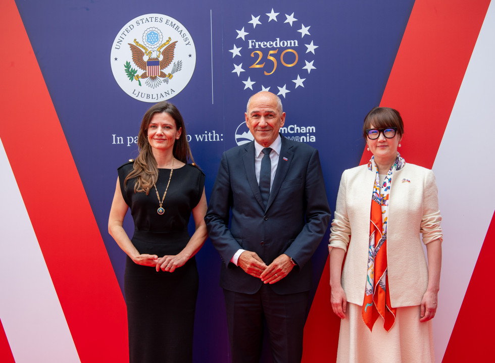 Urška Bačovnik Janša, Janez Janša, and Asel K. Roberts are standing, with American symbols in the background.