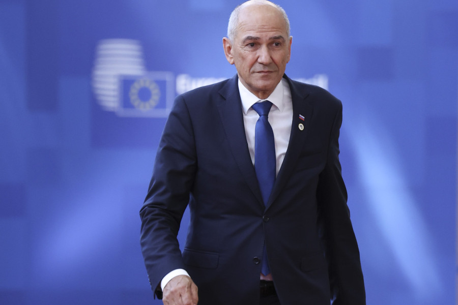 Moški v temni obleki in modri kravati hodi po prizorišču vrha Evropske unije, v ozadju je moder pano z zabrisanim logotipom Evropskega sveta.