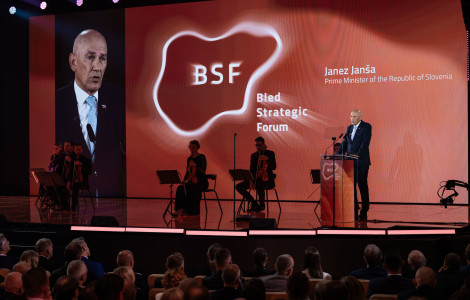 PV BSF 1 31082026 (Janez Janša is standing on the right behind the lectern; two musicians are seated in the centre; and on the right is a screen showing an image of Janez Janša. In the background, in the centre, are the symbols of the Bled Strategic Forum.)