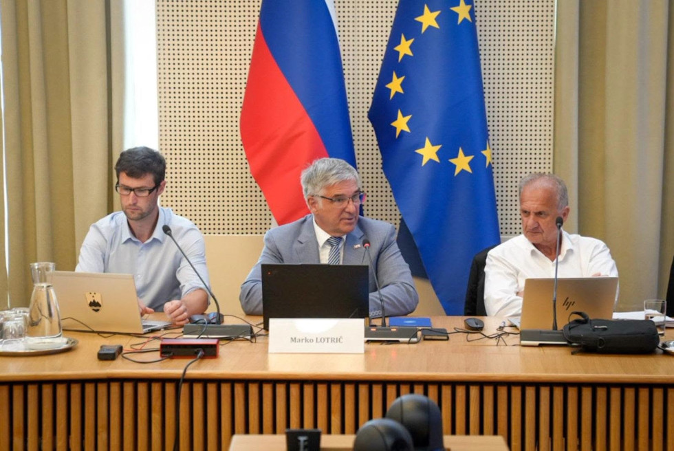 Tomaž Perše, Marko Lotrič in Ivan Simič sedijo za mizo, v ozadju so zastave. 
