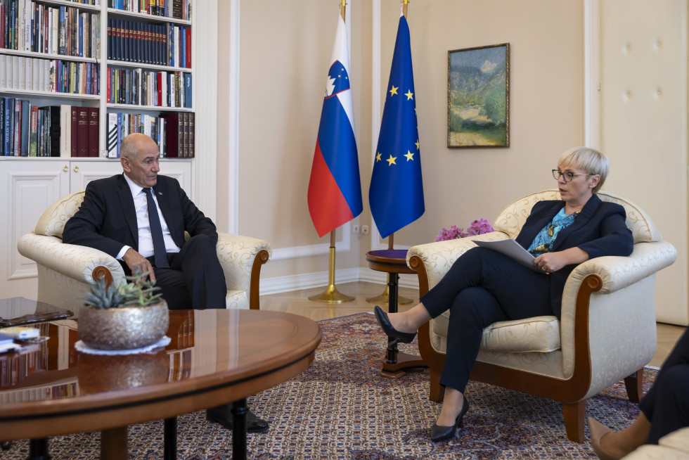 moški in ženska pred zastavama sedita v foteljih