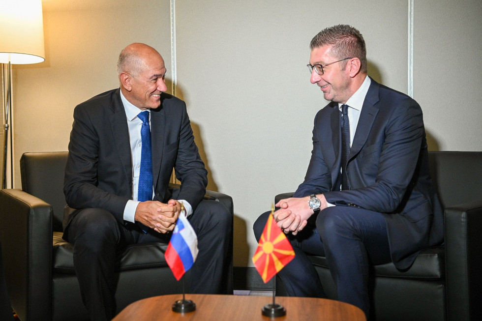 Dva moška v poslovnih oblekah sedita drug nasproti drugemu na dvostranskem srečanju, med njima pa sta na mizici slovenska zastava in zastava druge države.