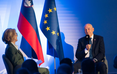 MK1 0765 (A seated man speaks into a microphone during a panel discussion beside Slovenian and European Union flags.)