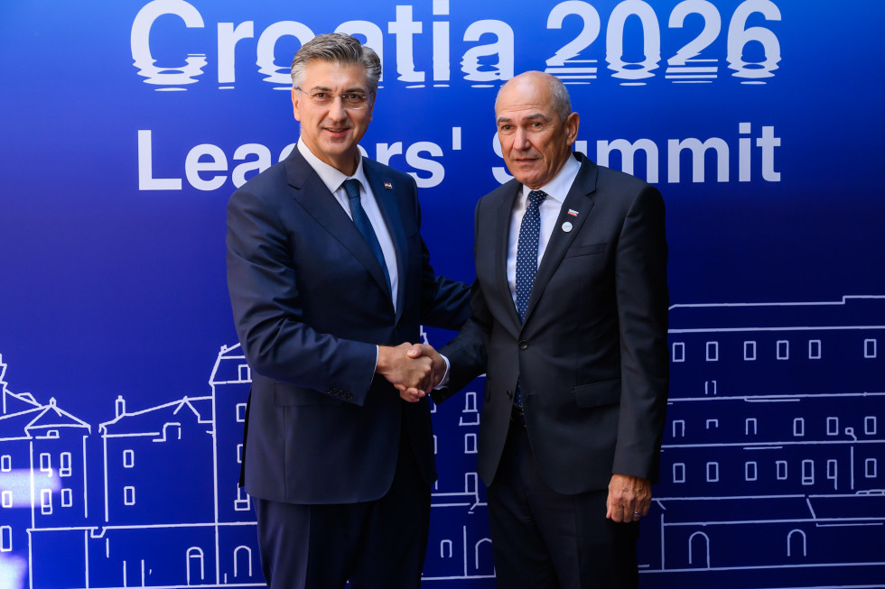 Janez Janša in Andrej Plenković se rokujeta, v ozadju so panoji s simboli Vrha MED9.