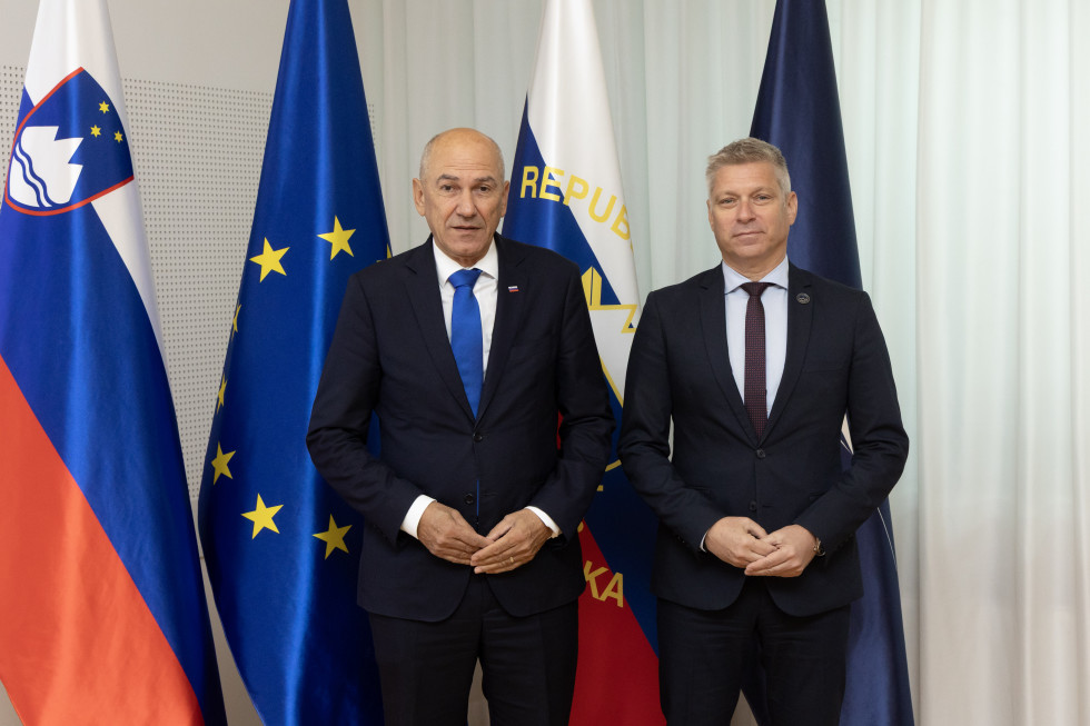Predsednik vlade in obrambni minister stojita pred zastavami