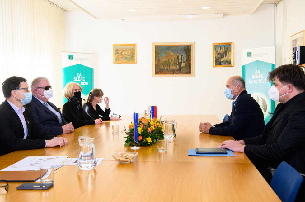 Predstavniki Zveze društev slepih in slabovidnih Slovenije in Janez Janša sedijo za mizo.