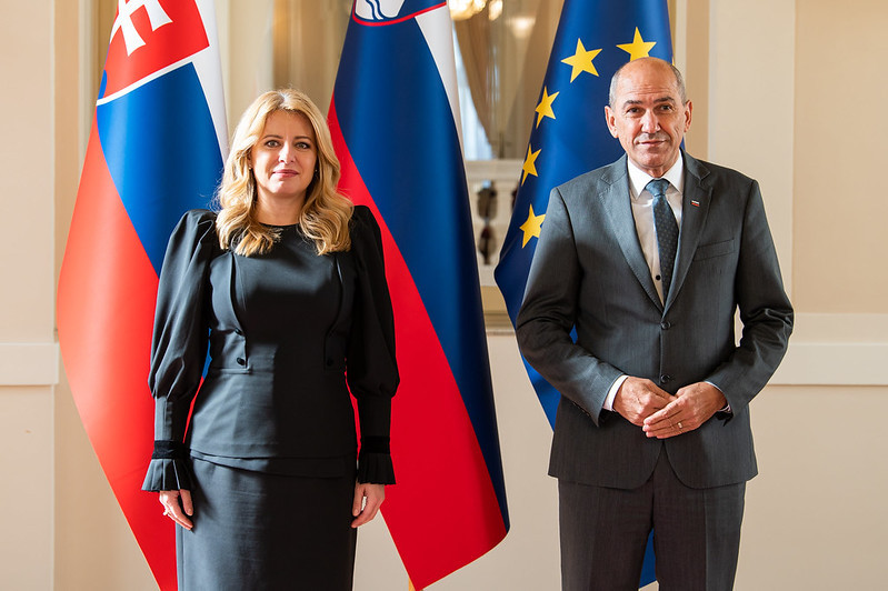 Predsednik vlade in predsednica Slovaške republike stojita pred zastavami.