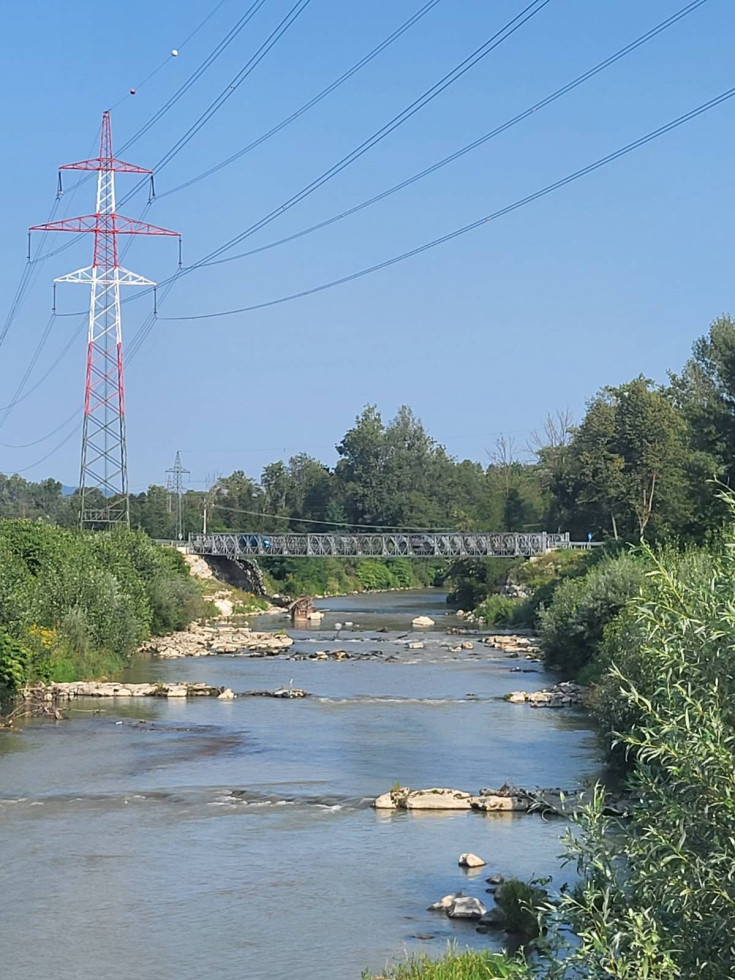Potok Mlinščica, ki teče skozi Dol pri Ljubljani. Preko potoka tečejo vodi za elektriko. Levo in desno sta z zelenjem poraščena bregova, na levi stoji drog električnega daljnovoda. Prek potoka je most.