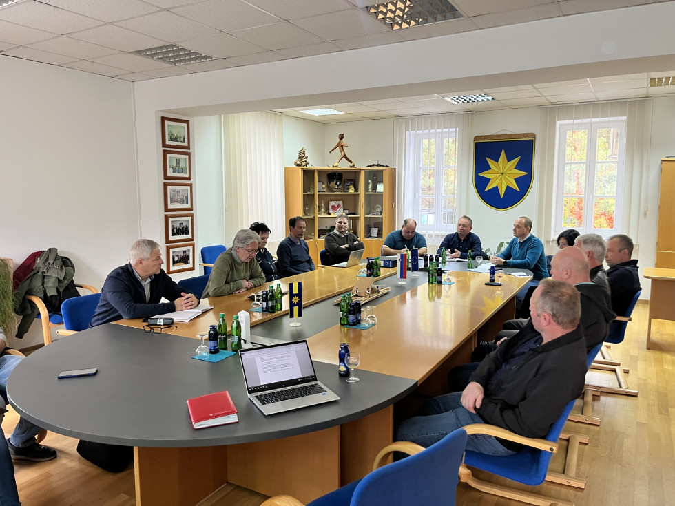 V občinski dvorani z grbom občine na steni med okni sedi za delovno mizo več oseb, med njimi državni sekretar Šefic in župan občine Ljubno ob Savinji