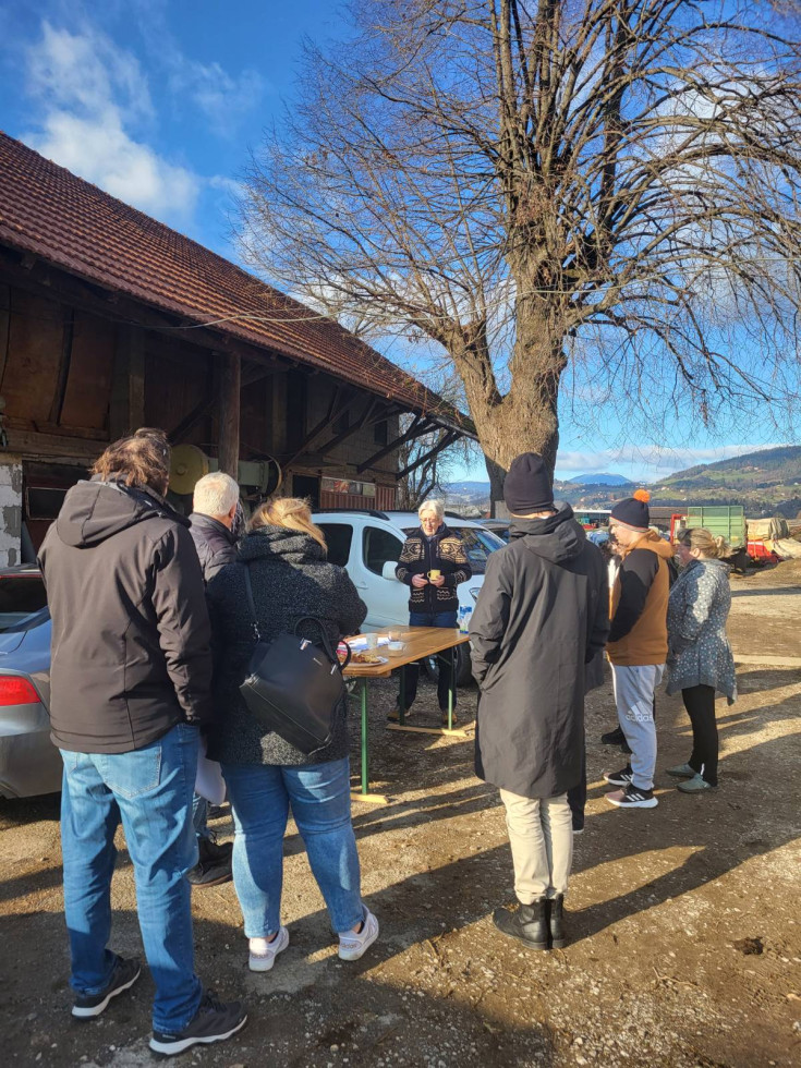 Ljudje stojijo in si ogledujejo hišo na levi ter brežino.