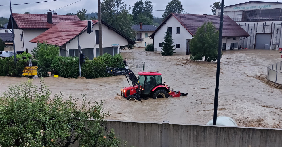 Houses stand in water during the 2023 floods, with a red tractor in the middle.