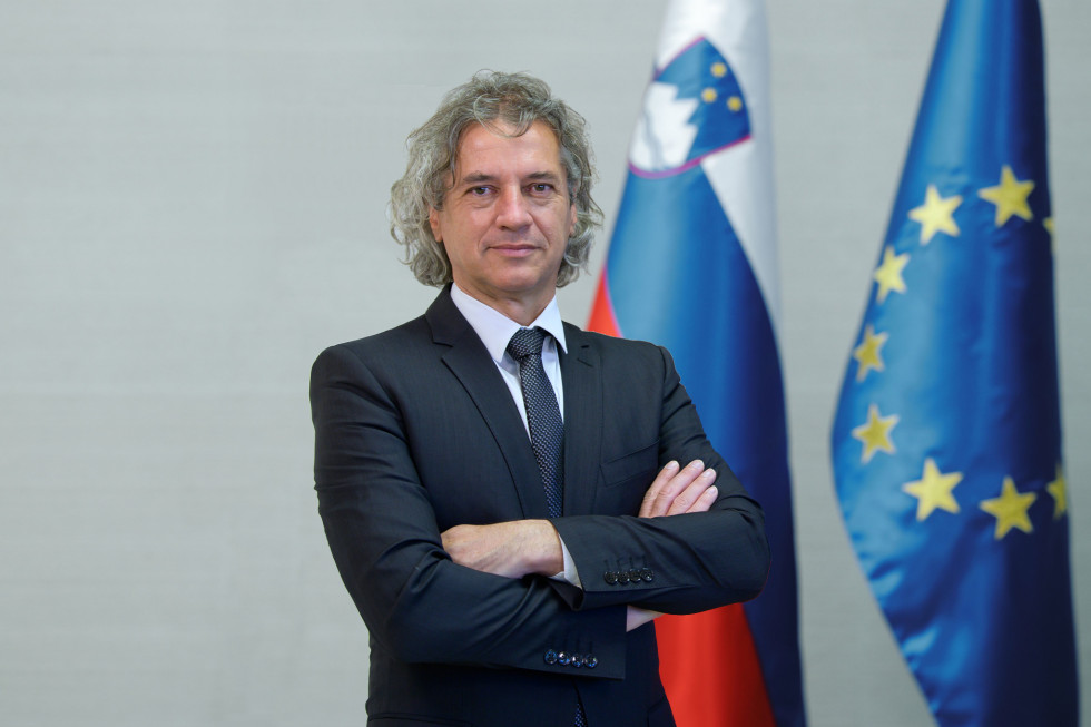 Portret dr. Roberta Goloba, v ozadju zastava Slovenije in EU