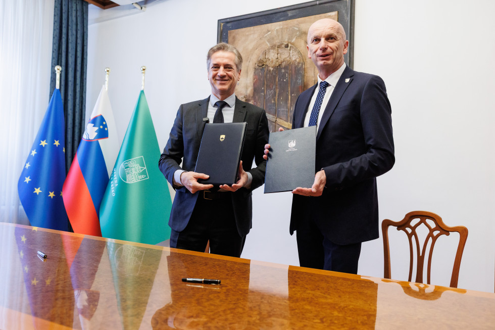 Moška stojita pred kamerami in v rokah držita pismo o nameri