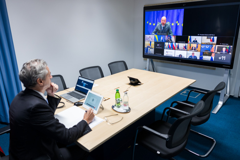 Predsednik vlade Robert Golob sedi za mizo, pred njim ekran z udeleženci zasedanja.