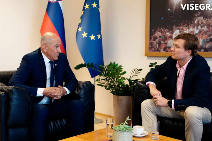 Dva moška sedita in se pogovarjata, za njima slovenska in zastava EU.