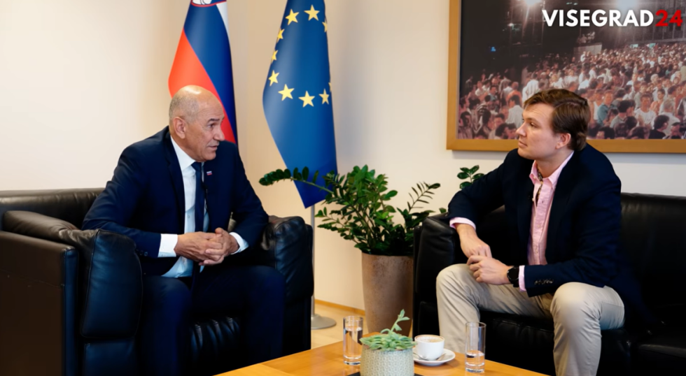 Dva moška sedita in se pogovarjata, za njima slovenska in zastava EU.
