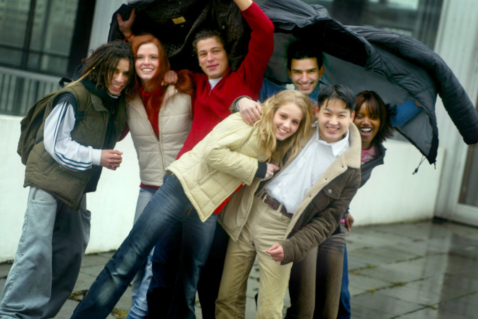 A group of young boys and girls are standing embraced in two rows and laughing.