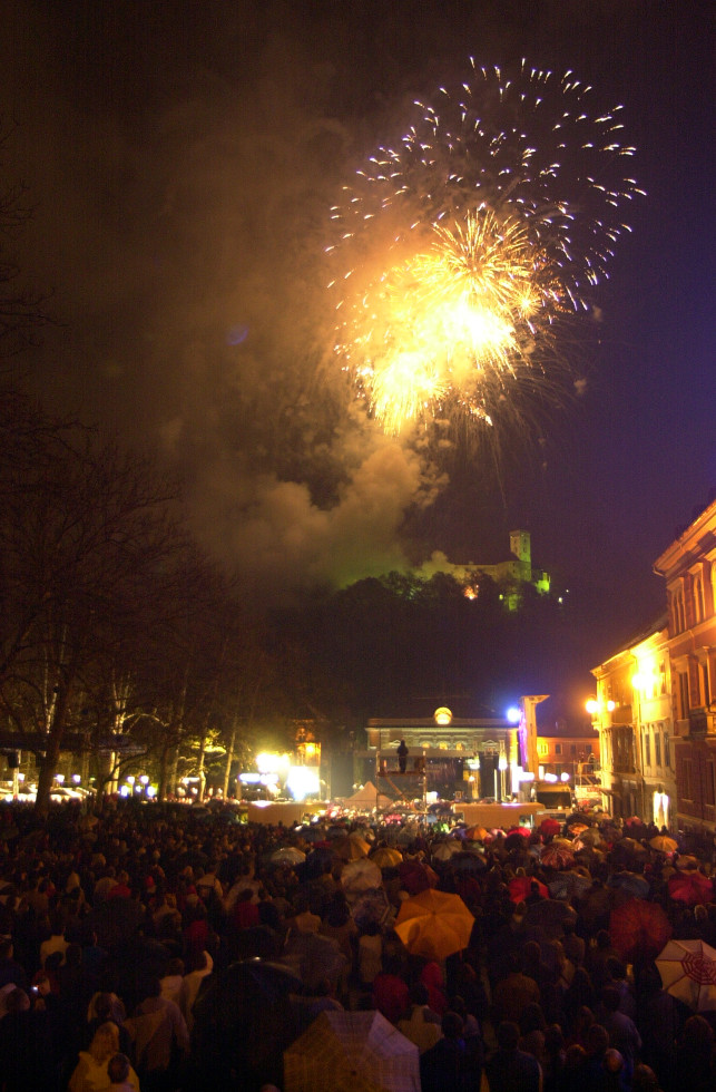 Ognjemet z ljubljanskega gradu, pod njim množica ljudi, nekateri imajo razprte dežnike.