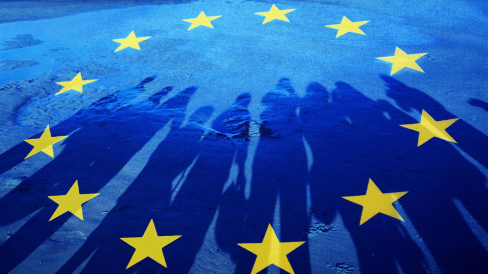 A circle of twelve yellow stars on a blue background, on the background are the shadows of people lined up.