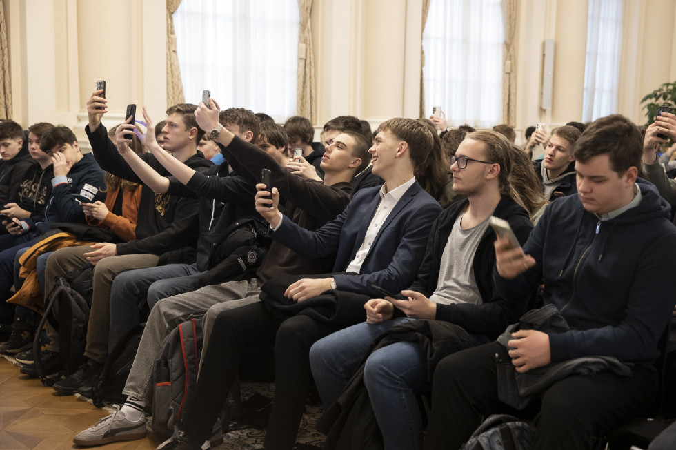 Mladi moški sedijo in v iztegnjenih rokah držijo mobilne telefone in slikajo.