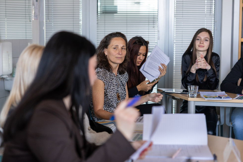 Fotografija s strani: ženske sedijo in gledajo naprej, ena pa gleda postrani in v objektiv.