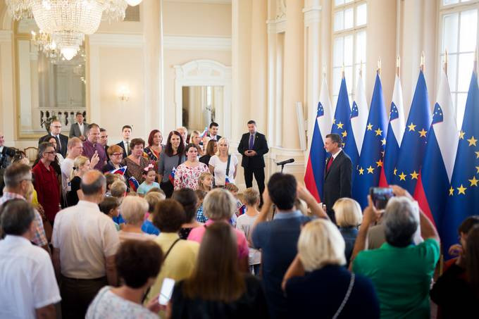 predsednik ob mikrofonu pred zastavami in zbrani gostje v veliki dvorani predsedniške palače