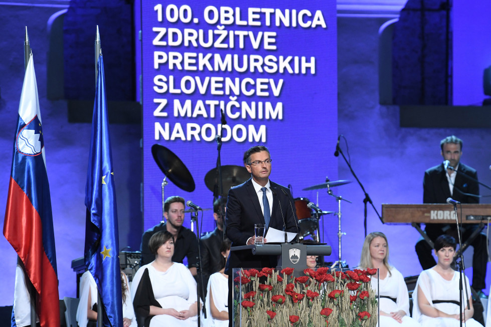 predsednik vlade ob govorniškem pultu na odru proslave v Beltincih, za njim del nastopajočih