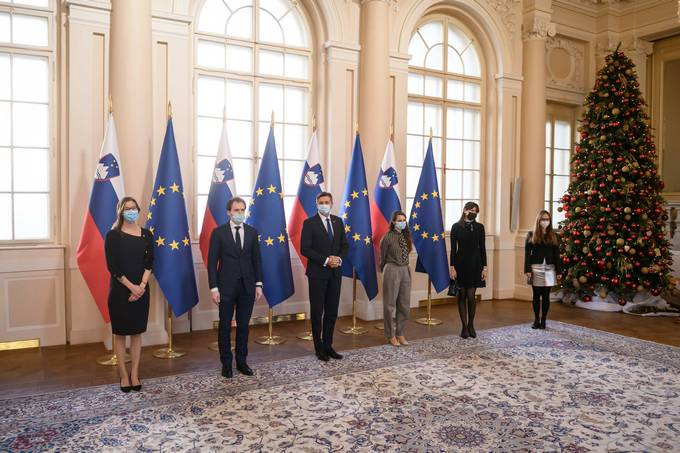 Člani društva VTIS stojijo s predsednikom republike pred zastavami v veliki dvorani predsedniške palače