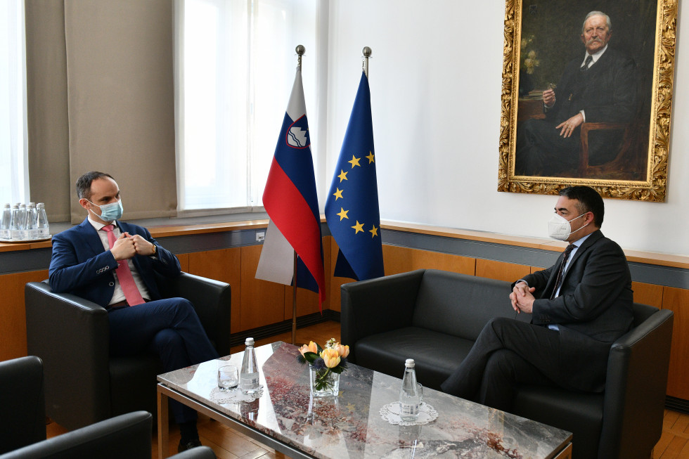 gost in gostitelj sedita na pogovorih v salonu, zadaj zastave