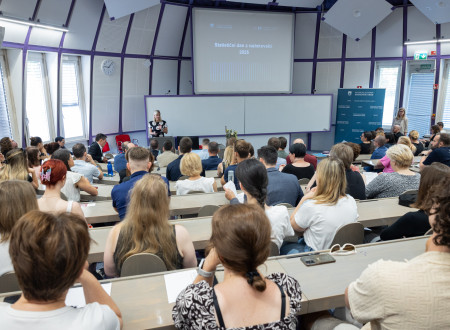 Udeleženci dogodka Statistični dan z raziskovalci 2025. Sedijo v dvorani, gledajo govornico. Ta stoji za govorniškim pultom.