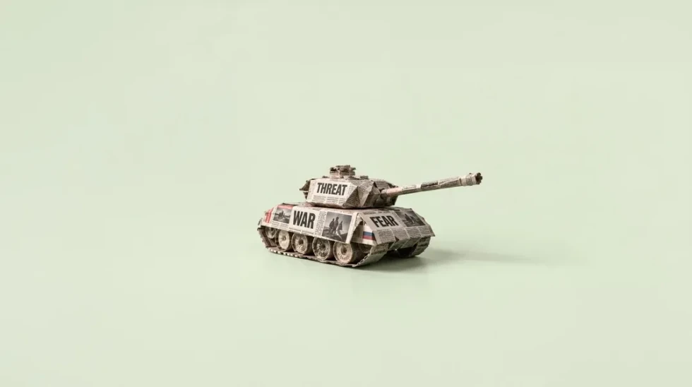 A toy tank constructed from newspaper, with the words “THREAT,” “WAR,” and “FEAR” printed on its side.