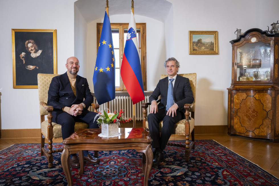 Charles Michel in Robert Golob sedita za mizico, med njima sta zastavi EU in RS.