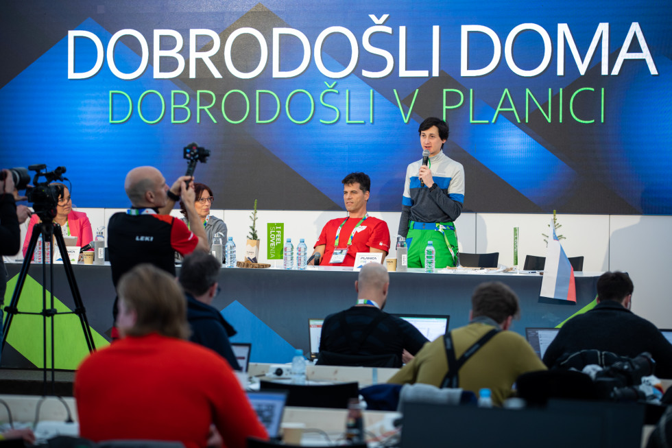 Fotografi fotografirajo, novinarji sedijo pred omizjem. Za omizjem sedita Mirjam Bizjak, Gregor Jurak, Cene Prevc stoji z mikrofonom v roki.