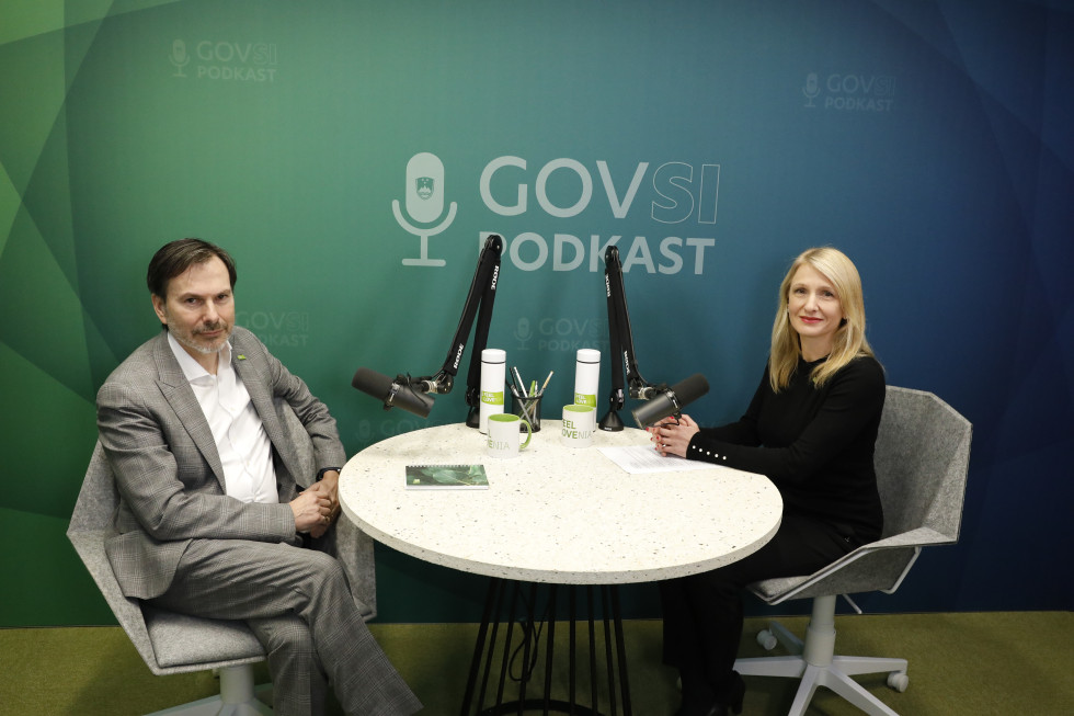 Moški in ženska sedita za okroglo mizo z mikrofonoma, v ozadju napis GOVSI podkast