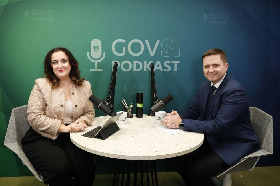 A woman and a man are sitting at a table, and behind them is the sign GOVSI Podcast.