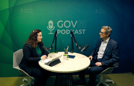 AZC9441 (A woman and a man sitting at a round table with microphones. Behind them is a green background with GOVSI podcast written on it.)