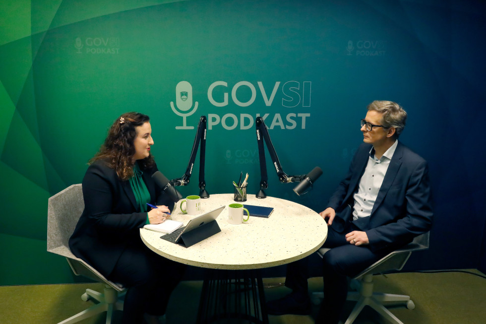 A woman and a man sitting at a round table with microphones. Behind them is a green background with GOVSI podcast written on it.