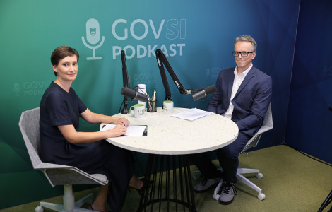 DK996934 (A woman and a man are seated at a round table with microphones, looking directly at the camera. Behind them, against a green background, is the text GOVSI Podcast.)