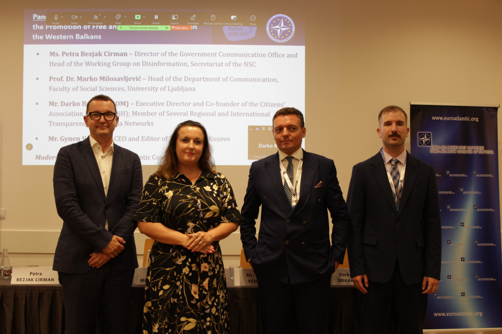 Trije govorci seminarja in moderator stojijo pred prezentacijo z njihovimi imeni
