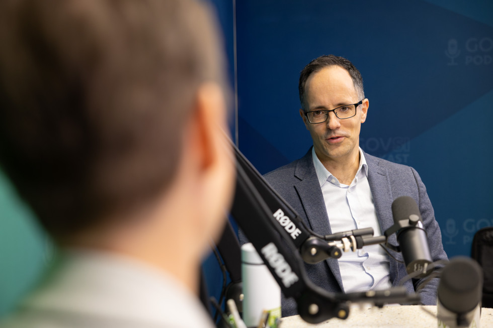 Moški sedi za mizo, pred njim mikrofon.