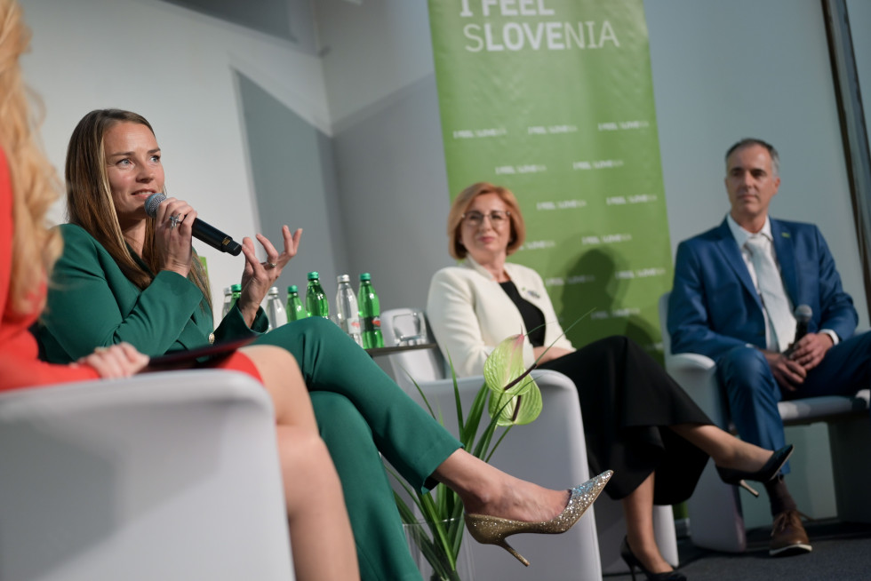 Tina Maze sits on stage and speaks into a microphone. Anita Stojčevska and Milan Hosta are sitting next to it.