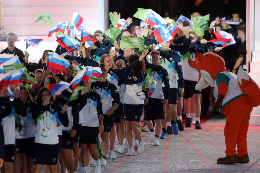 Mimohod športnikov z zastavicami I feel Slovenia in Republike Slovenije. Pozdravlja jih maskota Foksi.