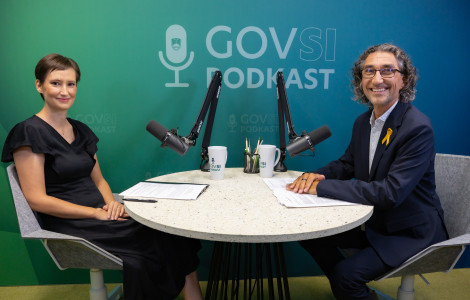 UKLS1471 (A woman and a man sit at a round table with microphones in a GOVSI PODKAST studio, smiling; papers and mugs on the table.)